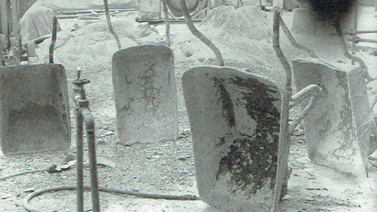 A black and white photo of wheelbarrows standing upright on a gravelly construction site.